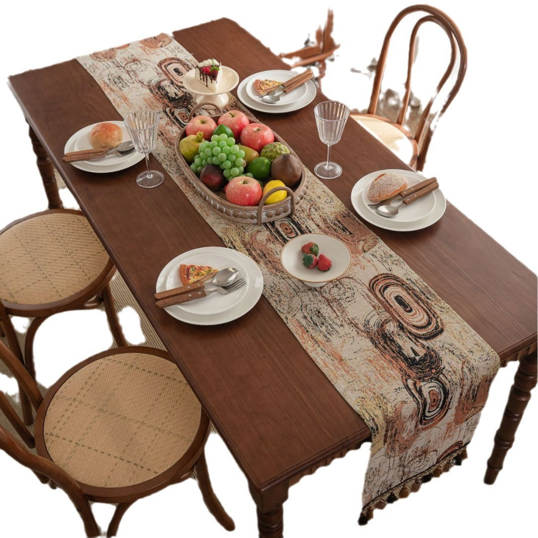 A rectangular wooden dining table set with plates, cutlery, glasses, a fruit bowl, and a decorative table runner, surrounded by wooden chairs on a plain white background.