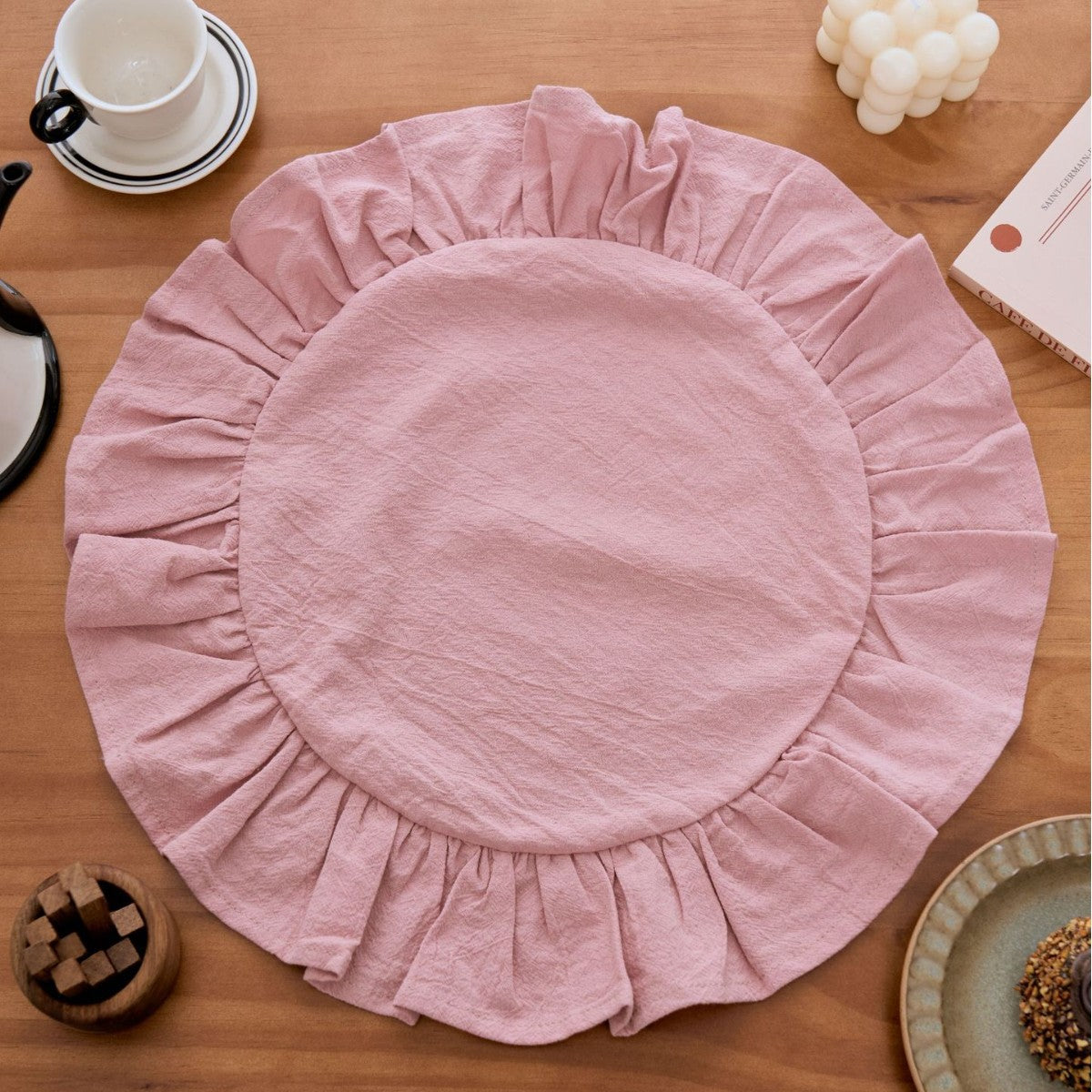 Pink round placemat with ruffled edge on a wooden table.