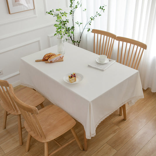 Dining table with a white tablecloth, wooden chairs, and a plant in a bright room.