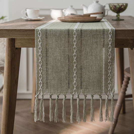 Green woven table runner with tassels on a wooden table.
