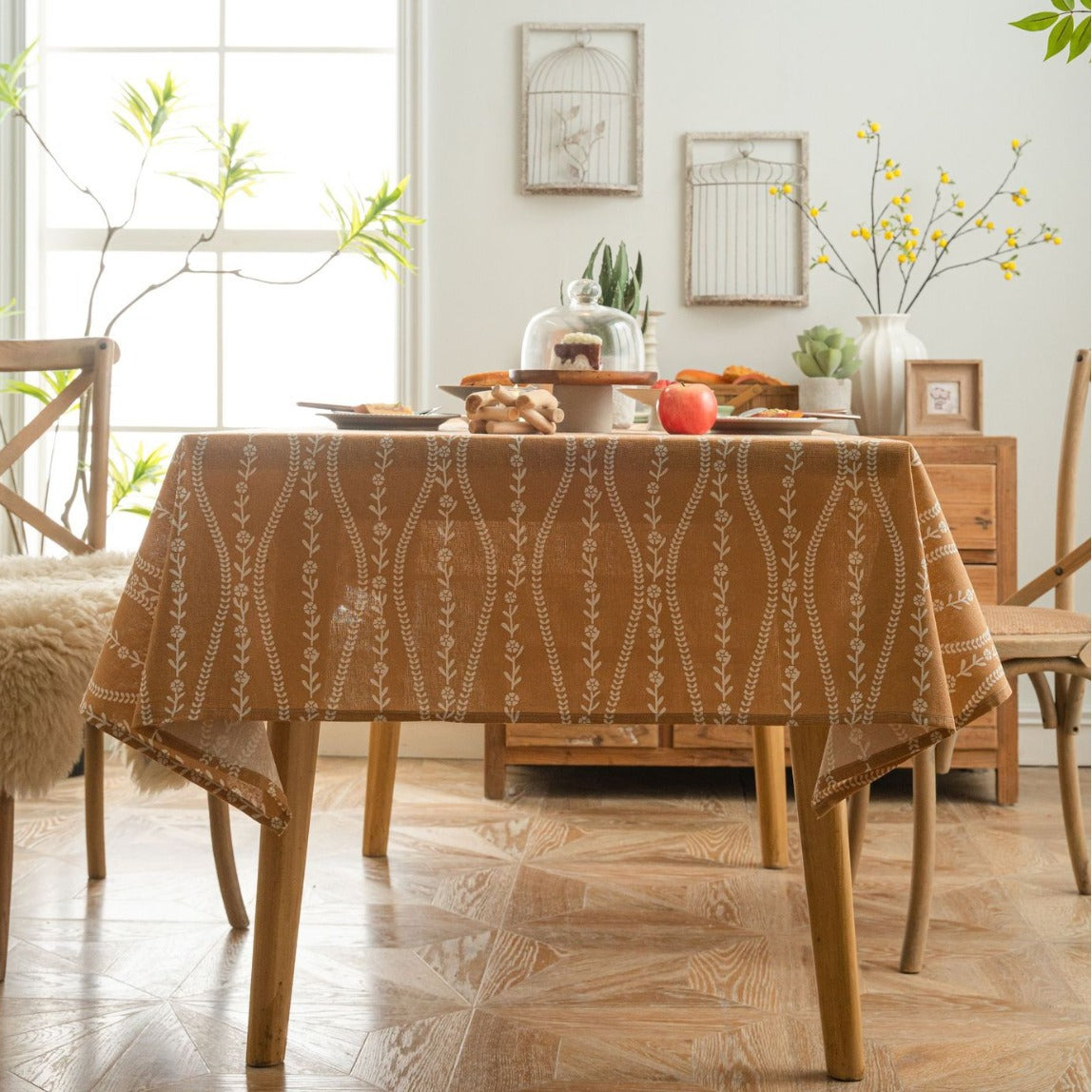 Dining room with a table covered by a patterned tablecloth, surrounded by chairs and decor.