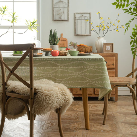 Dining room with a green patterned tablecloth on a wooden table, surrounded by chairs and decor.