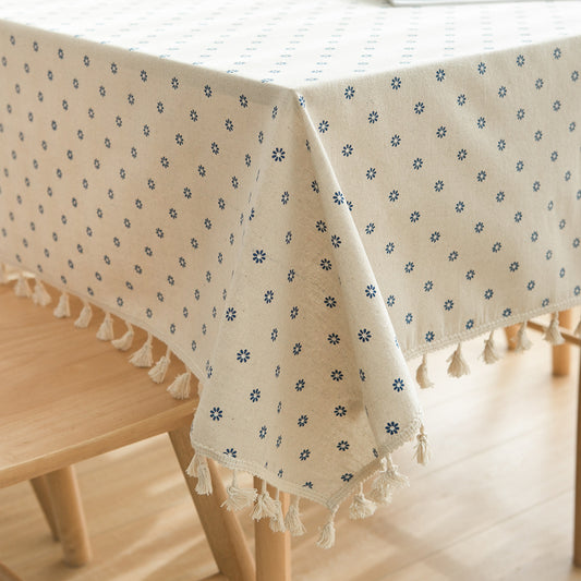 Beige tablecloth with floral pattern and tassels on a wooden table.