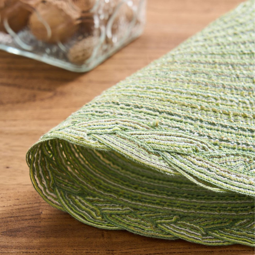 Green textured placemat on a wooden surface with a glass container in the background.