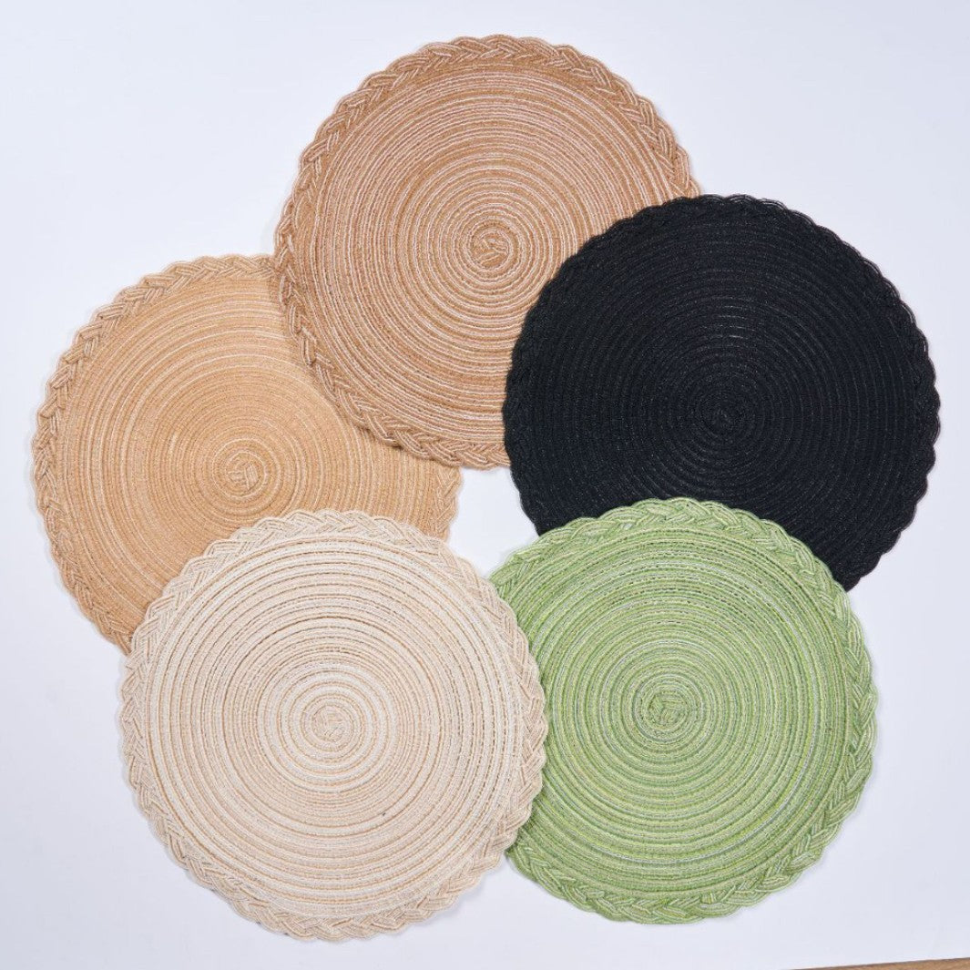 Five round braided woven placemats in natural beige, tan, black, cream, and sage green, arranged on a plain white background.