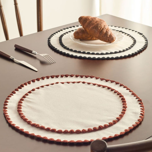 Round placemats with decorative edges on a table with a croissant.