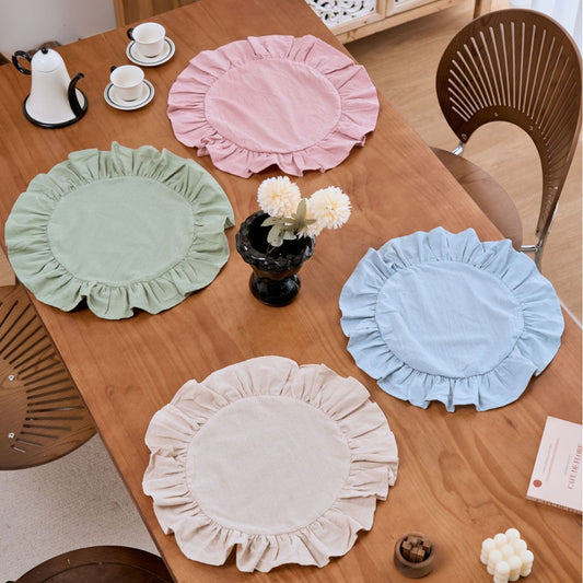 Four round placemats in pink, green, blue, and beige on a wooden table.